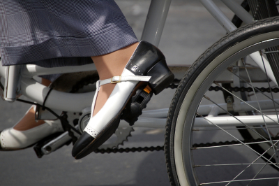 A woman cycling on a bicycle through city streets in business shoes and pants.