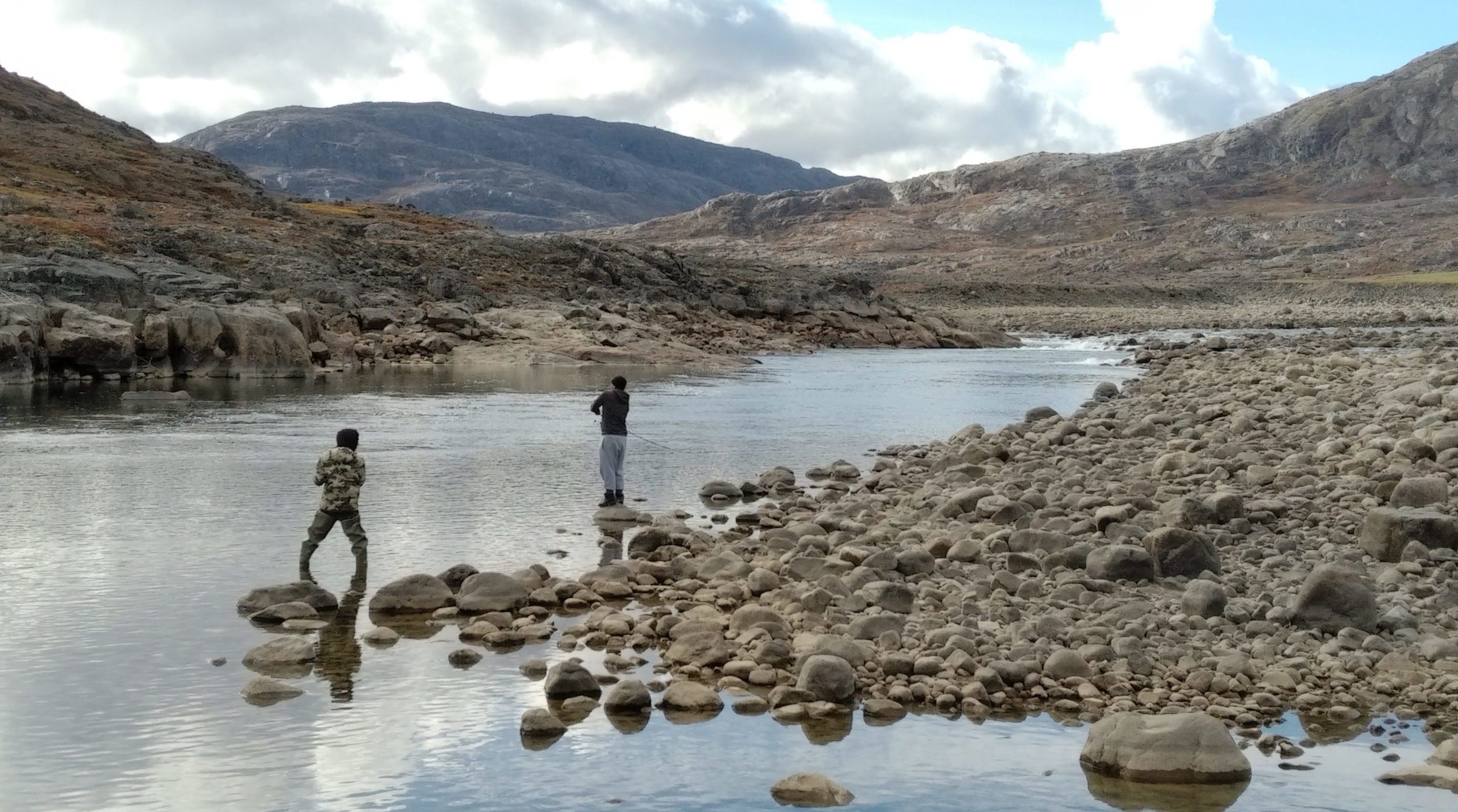 Two people doing a shoreline cleanup in Nungarut, Nunavut, with mountains in the background