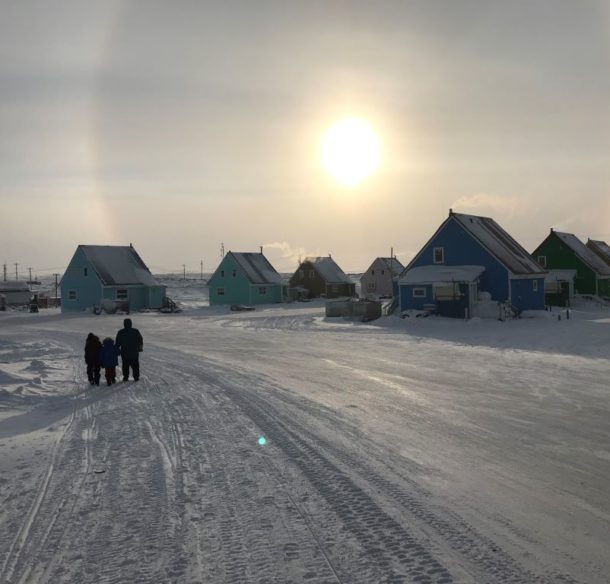 People walking under a sundog in a wintry Taloyoak, NU