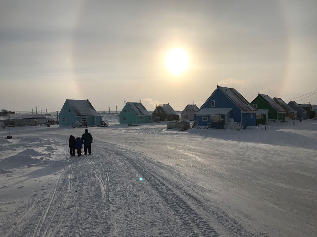 People walking under a sundog in a wintry Taloyoak, NU