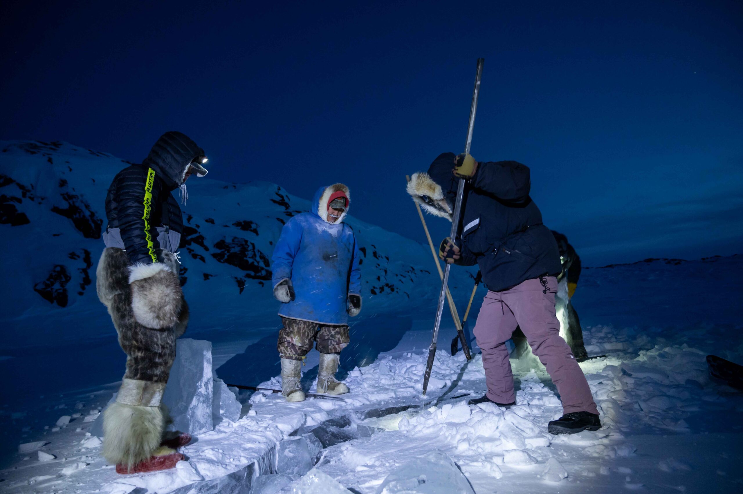 Three people standing on sea ice in Nunavut, one carrying a spear 