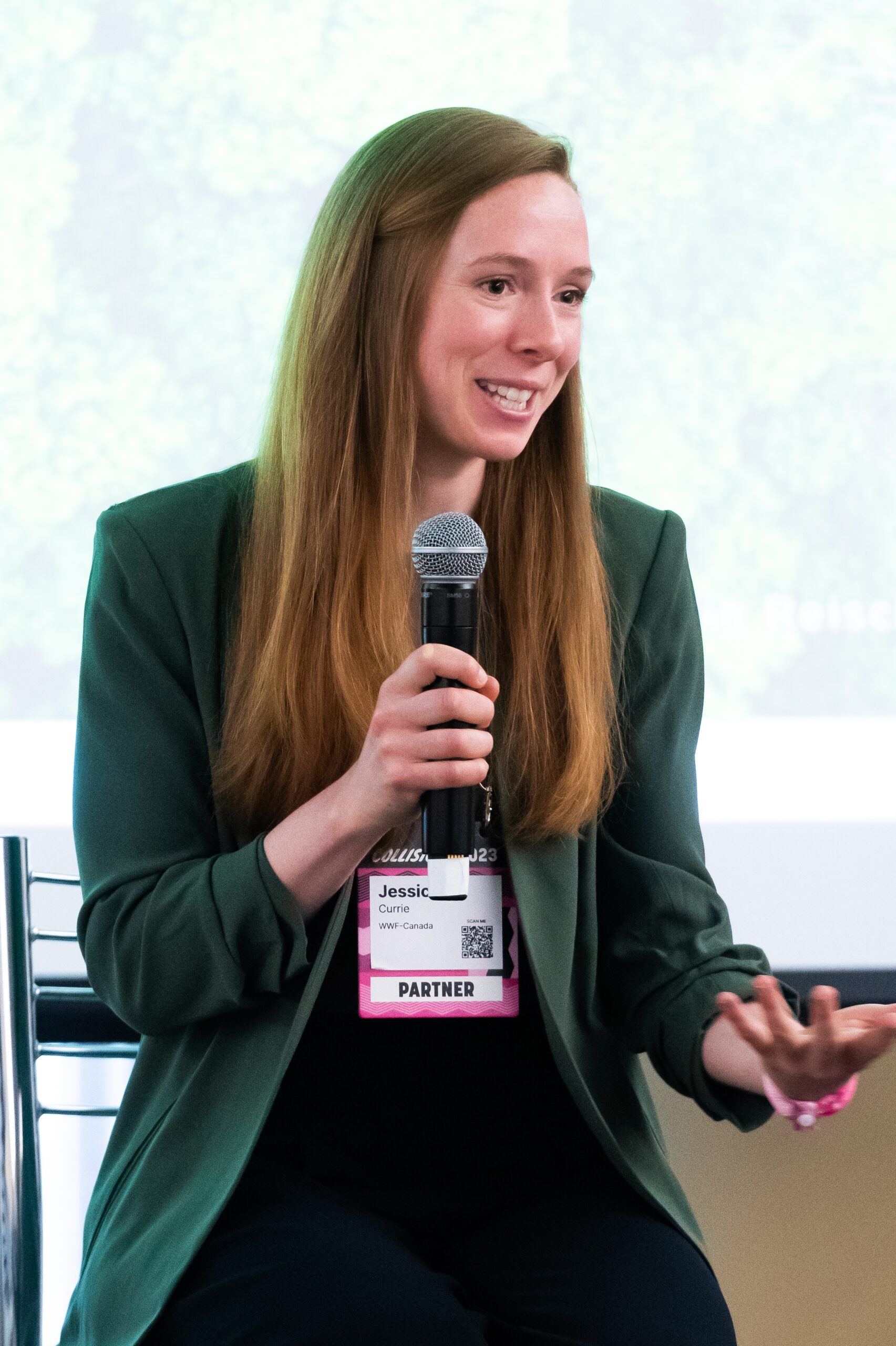 Woman in green jacket, seated, holding microphone