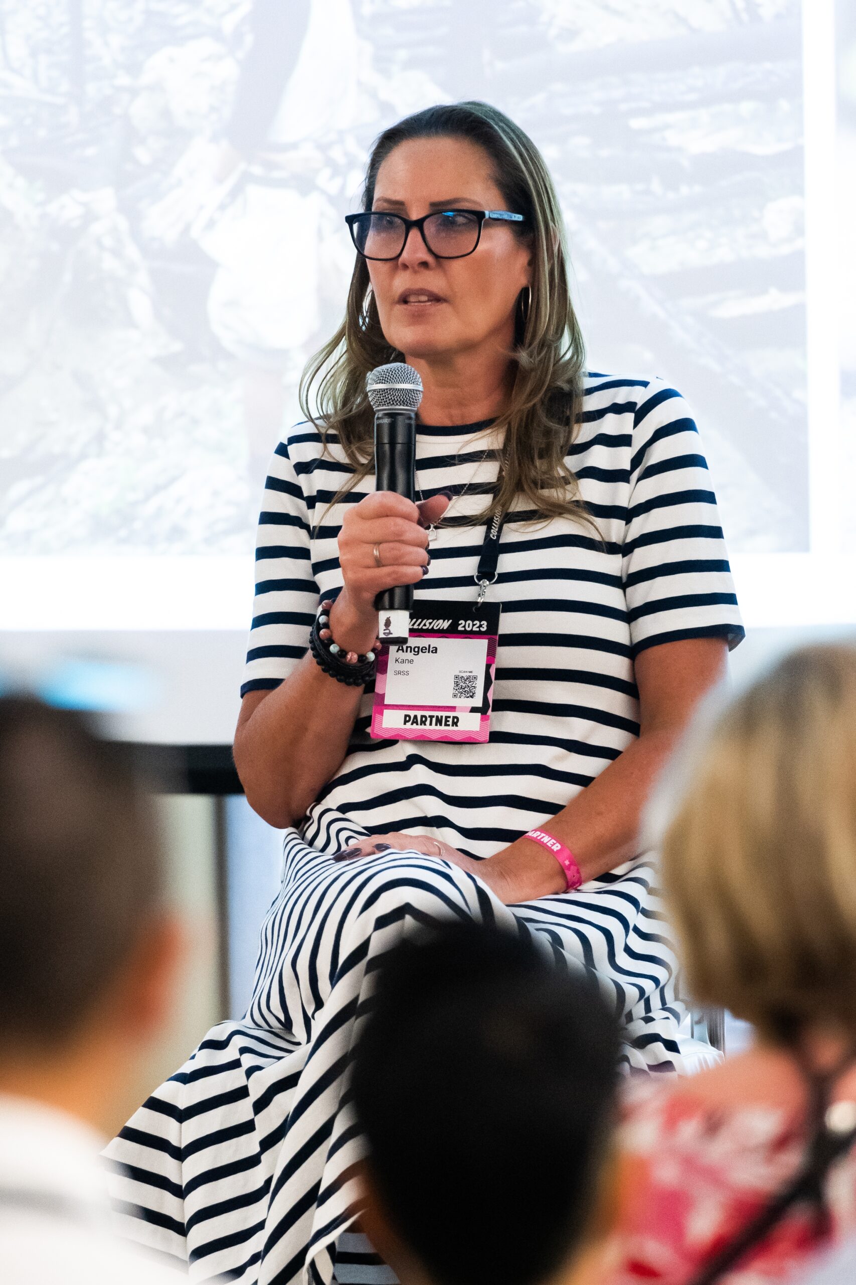 Indigenous woman in striped dress, seated holding a microphone