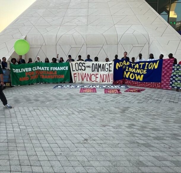 A group of people holding signs that say "deliver climate finance," "loss and damage finance now," and "adaptation finance now"