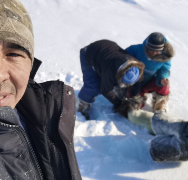 A man standing foreground with children behind him ice fishing