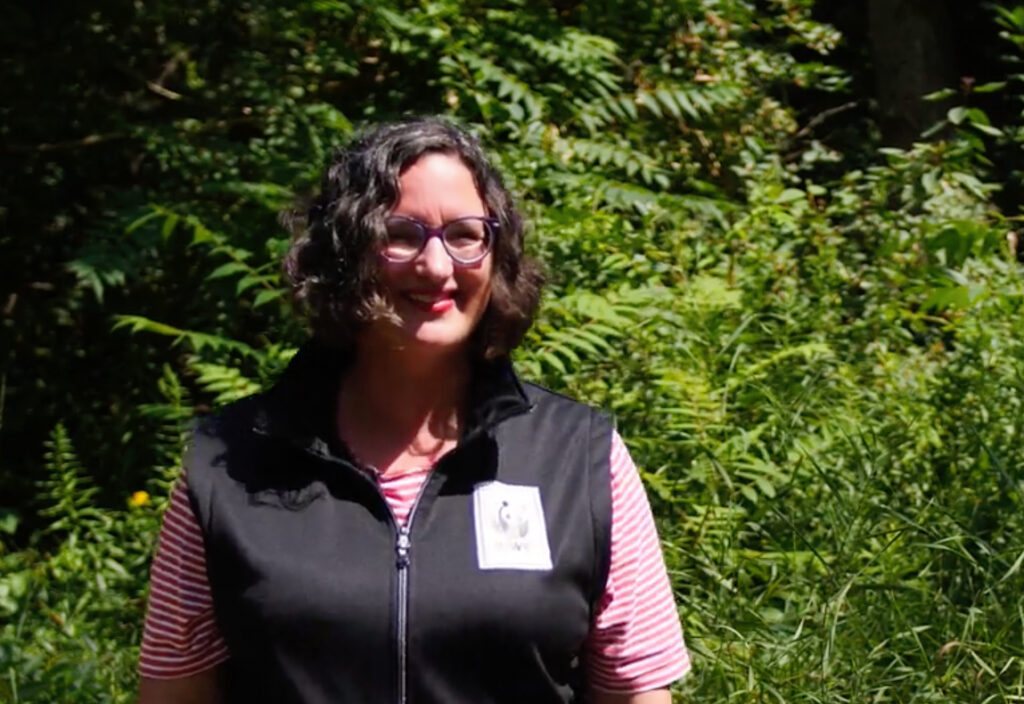 A woman smiling in front of trees and shrubs. 