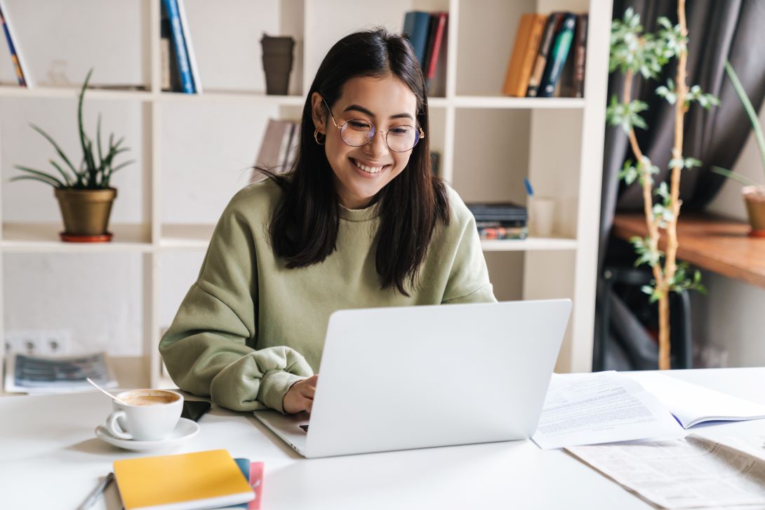 A person sitting at a desk smiling as they type on a laptop.