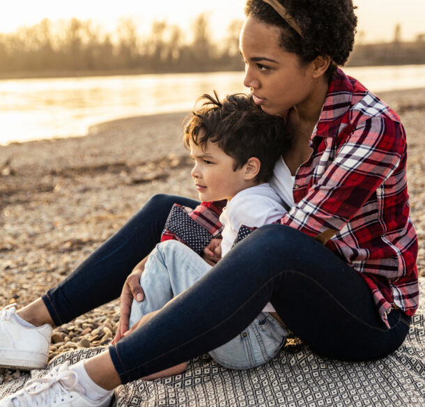 a woman sitting with a young child on a beach with the sun setting behind them