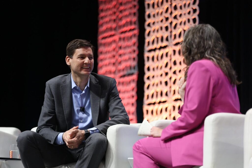 A man in a suit with a woman seen from behind both sitting in white chairs. 