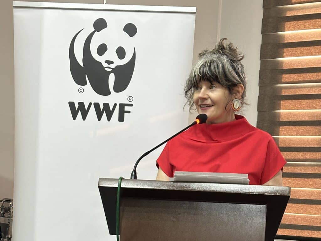 Une femme parle dans un micro sur un podium avec le logo du panda du WWF en arrière-plan.