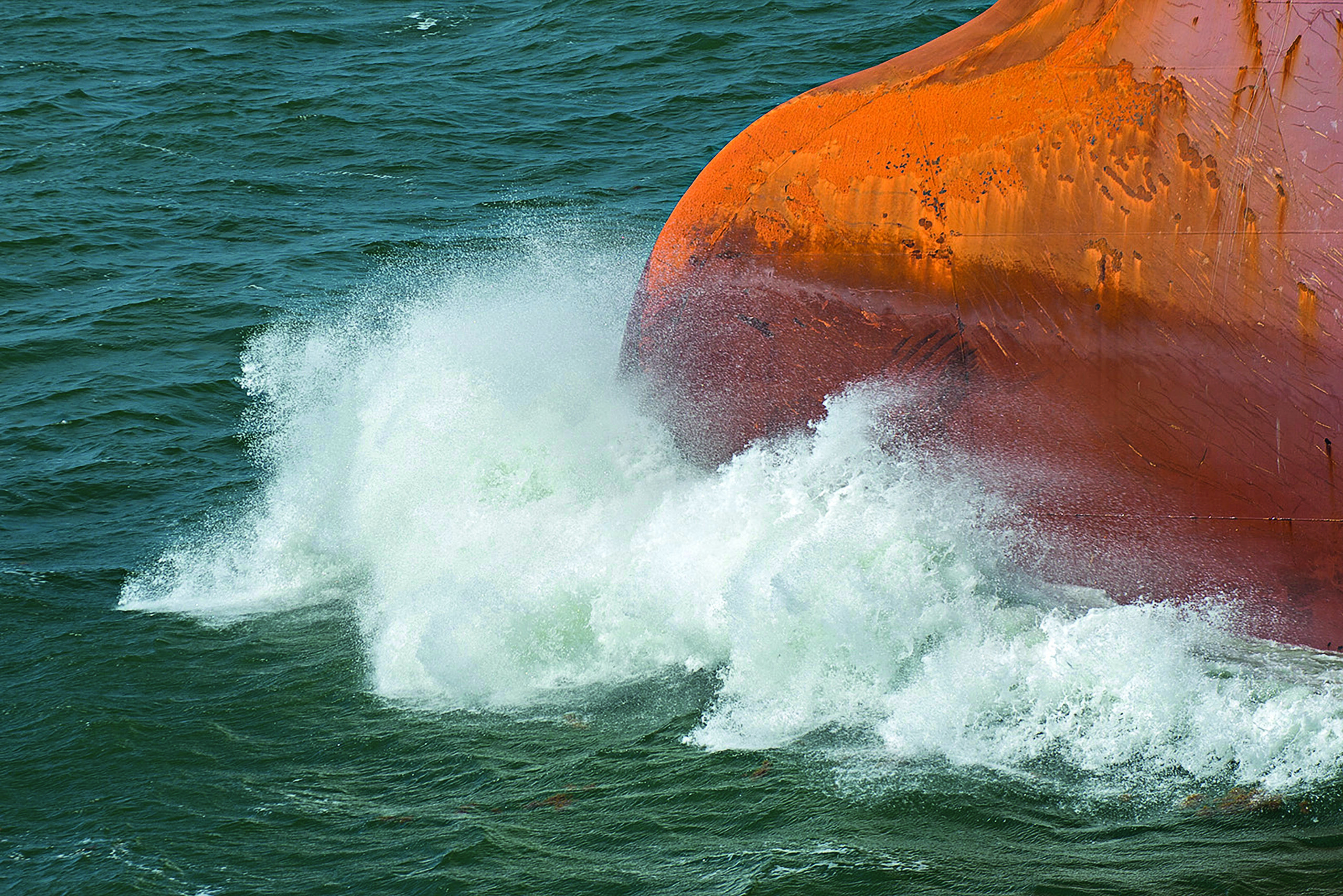 Ocean spray rises from the bow of a fast-moving bulk carrier.