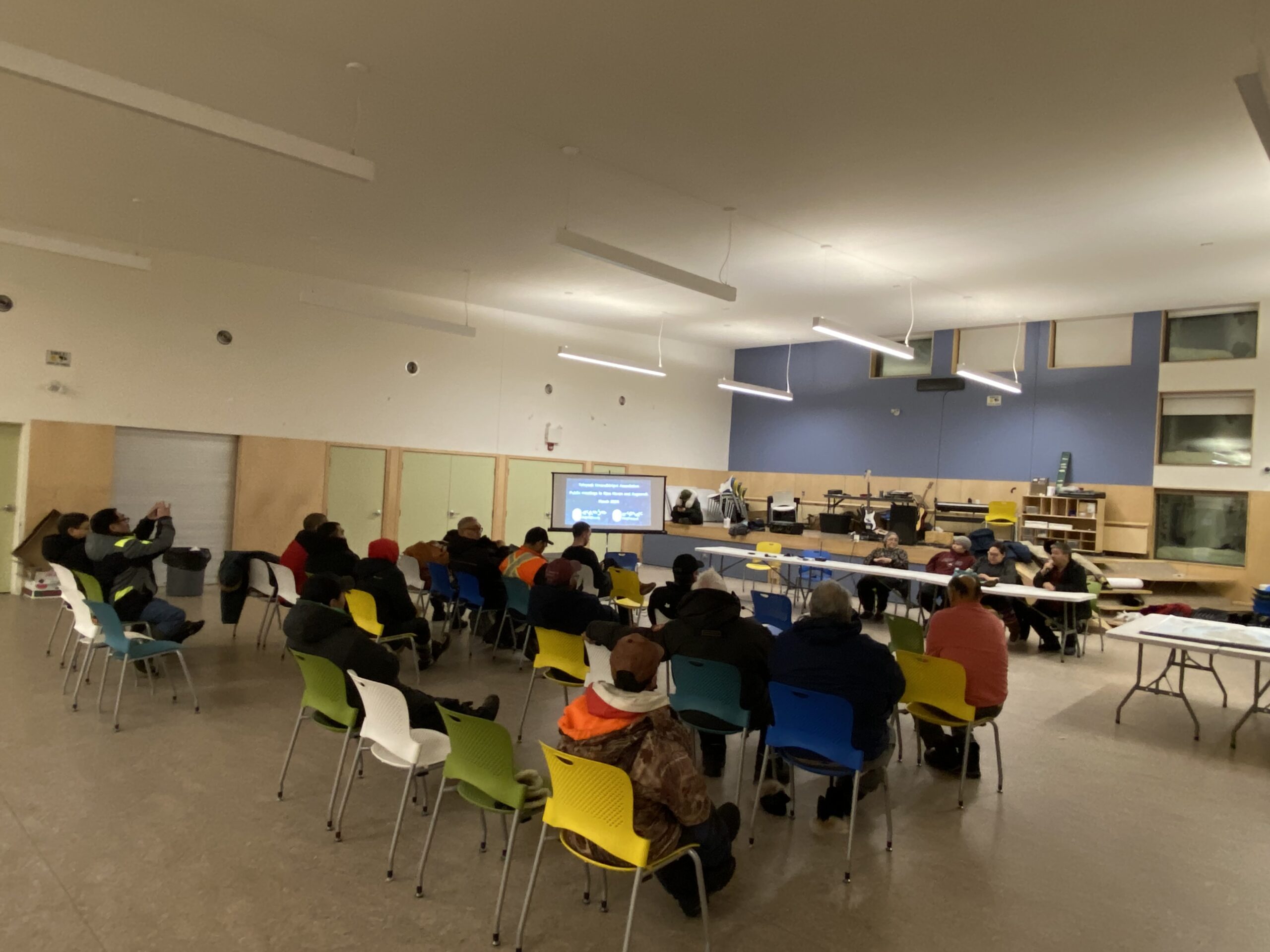 A large room full of people on chairs with presenters in the front at a long table